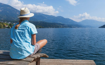 Frau sitzt auf Steg und blickt über einen See