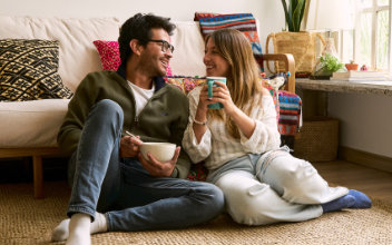 Paar sitzt zusammen im Wohnzimmer auf dem Boden und trinkt Kaffee