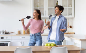 Fröhliches Paar benutzt Küchenutensilien als Mikrophon
